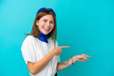 Uçak hostesi İngiliz kadın mavi arka planda izole edilmiş şaşırmış ve işaret ediyor.