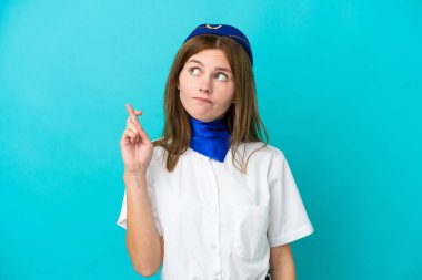 Uçak hostesi İngiliz kadın mavi arka planda izole edilmiş, parmakları çapraz ve en iyisini diliyor.