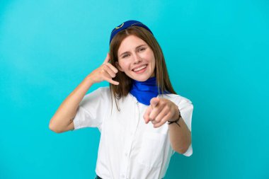 Uçak hostesi İngiliz kadın, mavi arka planda izole edilmiş, telefon jesti yapıyor ve ön tarafı işaret ediyor.