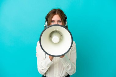 Tele pazarlamacı İngiliz kadın mavi arka planda izole edilmiş bir kulaklıkla çalışıyor megafonla bağırıyor.