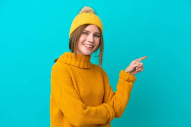 Kışlık ceket giyen genç bir İngiliz kadın mavi arka planda izole edilmiş.