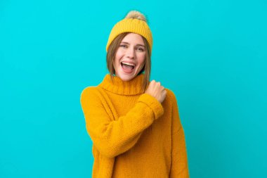 Mavi arka planda, zaferi kutlayan, kışlık ceket giyen genç İngiliz kadın.