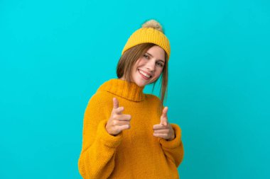 Kışlık ceket giyen genç İngiliz kadın, mavi arka planda izole edilmiş, ön tarafı gösteriyor ve gülümsüyor.