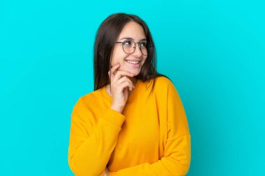 Genç Ukraynalı bir kadın mavi arka planda gözlüklü ve düşünürken yukarı bakıyor.