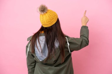 Pembe arka planda izole edilmiş kışlık ceket giyen genç Ukraynalı kadın işaret parmağıyla işaret ediyor.