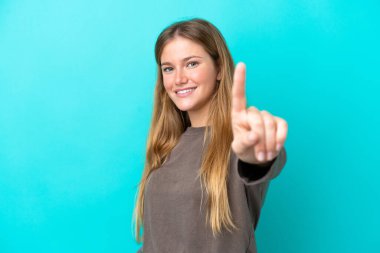 Mavi arka planda izole edilmiş genç sarışın kadın parmağını kaldırıyor ve gösteriyor.