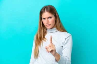 Mavi arka planda izole edilmiş genç sarışın kadın hayal kırıklığına uğramış ve ön tarafı işaret ediyor.