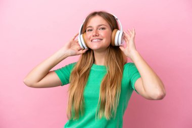 Pembe arka planda izole edilmiş genç sarışın kadın müzik dinliyor.