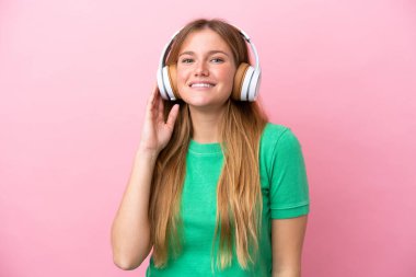 Pembe arka planda izole edilmiş genç sarışın kadın müzik dinliyor.