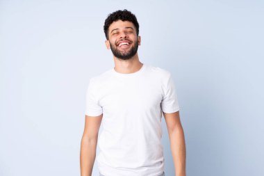 Genç Faslı adam mavi arka planda izole edilmiş gülüyor.