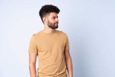 Faslı genç bir adam mavi arka planda izole edilmiş, yana bakıyor.