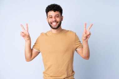 Mavi arka planda izole edilmiş genç Faslı iki elle zafer işareti gösteriyor.