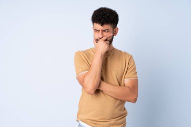 Faslı genç bir adam mavi arka planda izole edilmiş. Şüpheleri var ve kafası karışmış bir yüz ifadesi var.