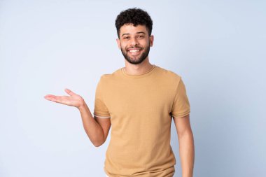 Faslı genç bir adam mavi arka planda izole edilmiş. Avucunda hayali bir şey tutuyor. Bir ilan vermek için.