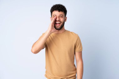Faslı genç bir adam mavi arka planda izole edilmiş ağzı açık bağırıyor.