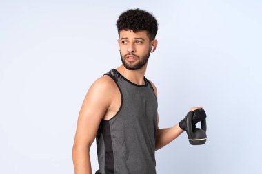 Faslı genç adam mavi arka planda izole edilmiş halter olarak ağırlık kaldırıyor.