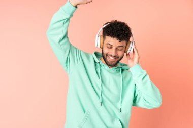 Genç Faslı adam pembe arka planda izole edilmiş müzik ve dans dinliyor.