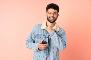 Pembe arka planda izole edilmiş cep telefonu kullanan genç Faslı bir adam zaferi kutluyor.