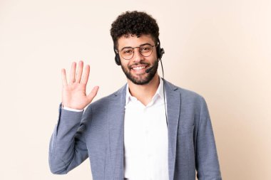 Faslı bir pazarlamacı bej arka planda izole edilmiş bir kulaklıkla çalışıyor. Mutlu bir ifadeyle selamlıyor.