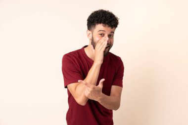 Bej arka planda izole edilmiş genç Faslı bir adam bir ürün sunmak ve bir şeyler fısıldamak için kenarı işaret ediyor.