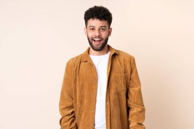 Faslı genç bir adam bej arka planda izole edilmiş ve yüzünde sürpriz bir ifade var.