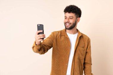 Bej arka planda izole edilmiş Faslı genç bir adam selfie çekiyor.