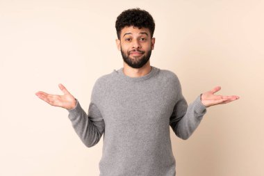 Faslı genç bir adam bej arka planda izole edilmiş. El kaldırırken şüpheleri var.