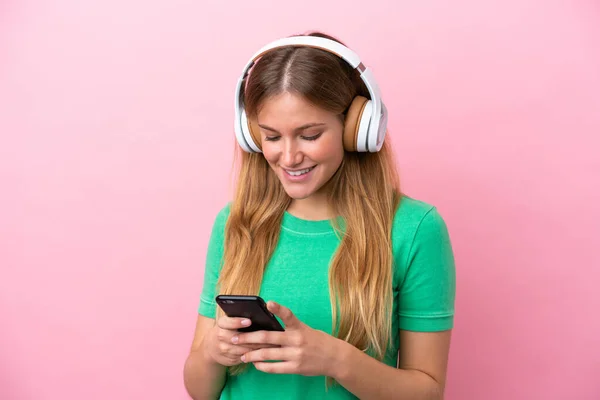 若いですブロンド女性絶縁上のピンクの背景リスニング音楽と見ますへモバイル — ストック写真
