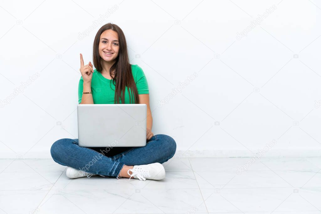 Young Ukrainian woman with a laptop sitting on floor showing and lifting a finger in sign of the best