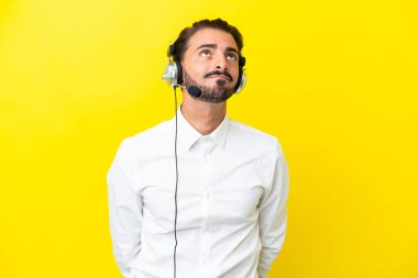 Tele pazarlamacı beyaz adam sarı arka planda izole edilmiş bir kulaklıkla çalışıyor.