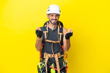 Kafkasyalı genç dağcı sarı arka planda izole edilmiş para hareketi yapıyor.