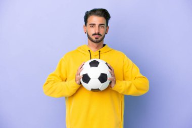 Mor arka planda futbol topuyla izole edilmiş genç beyaz bir adam.