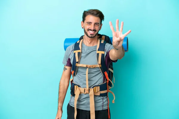 年轻的登山者 背着一个蓝色背景的大背包 快乐地数着四个手指 — 图库照片