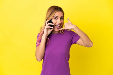 İzole edilmiş sarı arka planda cep telefonu kullanan genç bir kadın telefon hareketi yapıyor. Bana geri dönüş işareti ver.