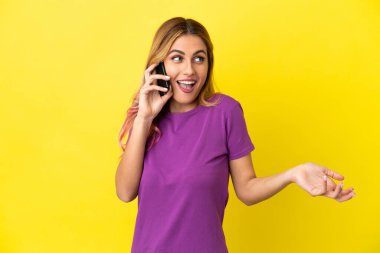 İzole edilmiş sarı arka plan üzerinde cep telefonu kullanan genç bir kadın.