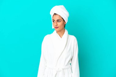 Bornozlu genç bir kadın izole edilmiş mavi arka planda yan tarafa bakıyor.