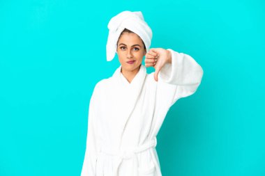 İzole edilmiş mavi arka planda bornozlu genç bir kadın olumsuz bir ifadeyle baş parmağını aşağı gösteriyor.