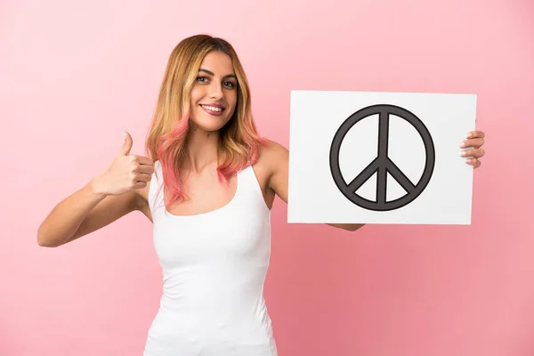 Молода Жінка Над Ізольованим Рожевим Тлом Тримає Плакат Символом Миру — стокове фото