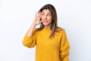 Beyaz arka planda izole edilmiş orta yaşlı beyaz kadın elini kulağına koyarak bir şeyler dinliyor.