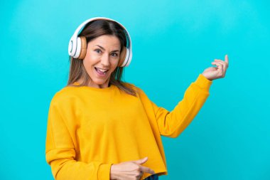 Orta yaşlı beyaz kadın mavi arka planda izole edilmiş müzik dinliyor ve gitar hareketi yapıyor.