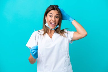 Mavi arka planda, sürpriz bir ifadeyle izole edilmiş orta yaşlı doktor kadın.