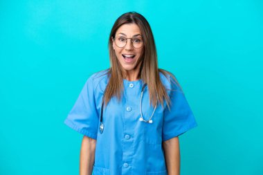 Orta yaşlı cerrah kadın, mavi arka planda, şaşırmış yüz ifadesi ile izole edilmiş.