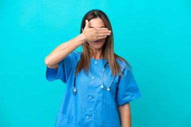 Orta yaşlı cerrah kadın mavi arka planda tek başına gözlerini elleriyle kapatıyor. Bir şey görmek istemiyorum.