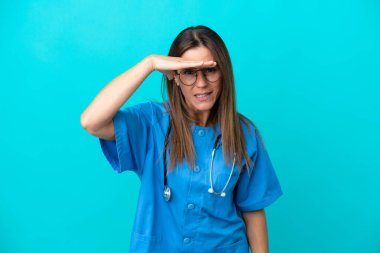 Orta yaşlı cerrah kadın, mavi arka planda izole edilmiş. Bir şeye bakmak için uzaklara bakıyor.