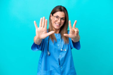 Mavi arka planda izole edilmiş orta yaşlı cerrah kadın parmaklarıyla sekiz sayıyor.