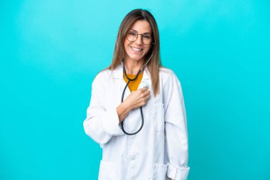 Mavi arka planda izole edilmiş orta yaşlı kadın doktor önlüğü giyiyor ve steteskop kullanıyor.