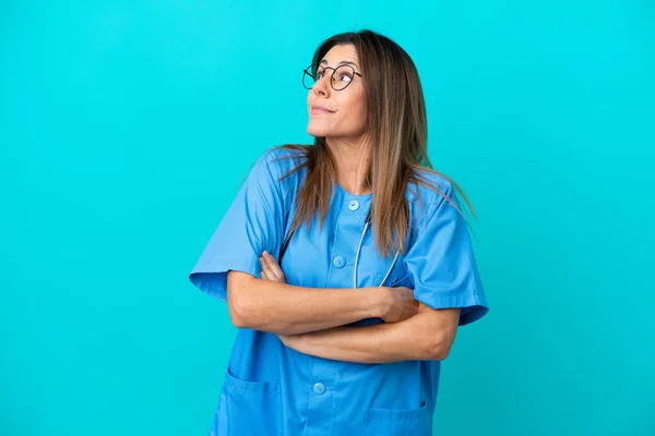 Chirurg Średnim Wieku Kobieta Odizolowany Niebieskim Tle Wątpliwość Gest Podczas — Zdjęcie stockowe