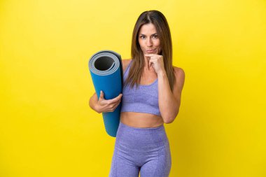 Elinde paspas tutarken yoga derslerine giden sporcu kadın sarı olmayan bir arka plan düşünüyor.