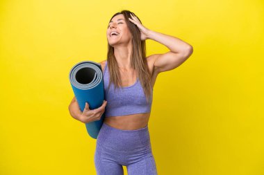 Spor kadını yoga derslerine giderken elinde sarı olmayan bir minder tutarken çok gülümsüyor.