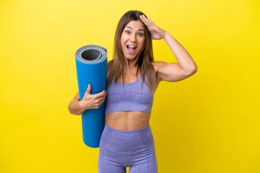 Elinde paspas tutarken yoga derslerine giden sporcu kadın sürpriz ifadesiyle sarı olmayan bir arkaplan tutuyor.